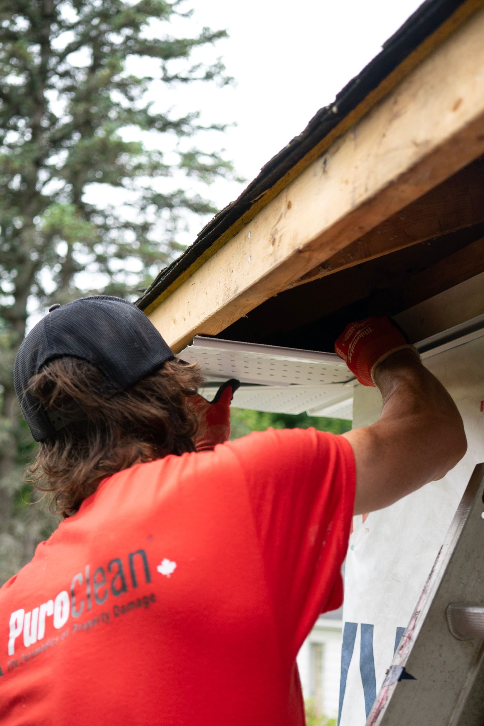 A worker repairing a roofline gutter from a ladder