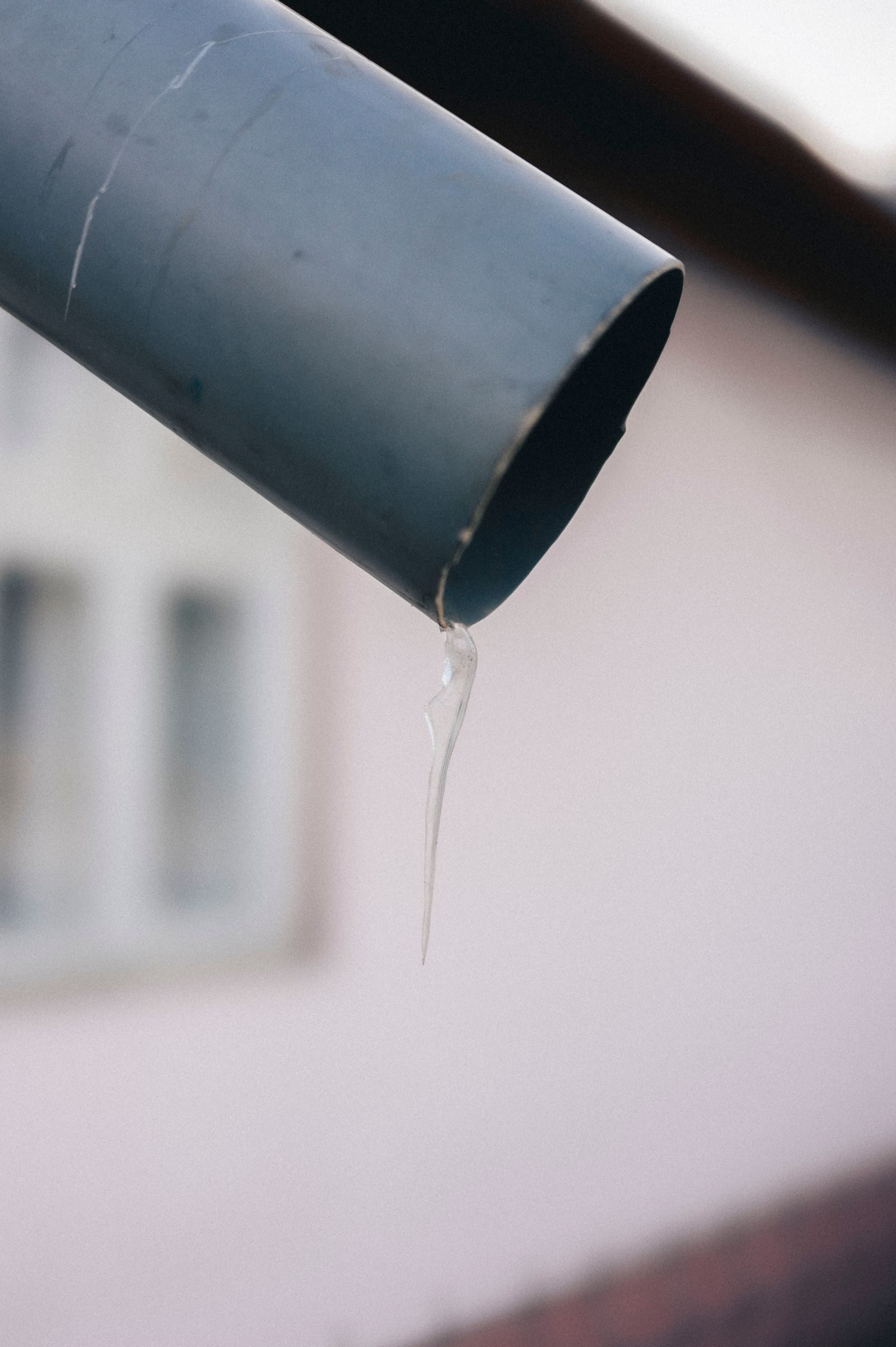 A gutter outlet and downpipe with a drip of water